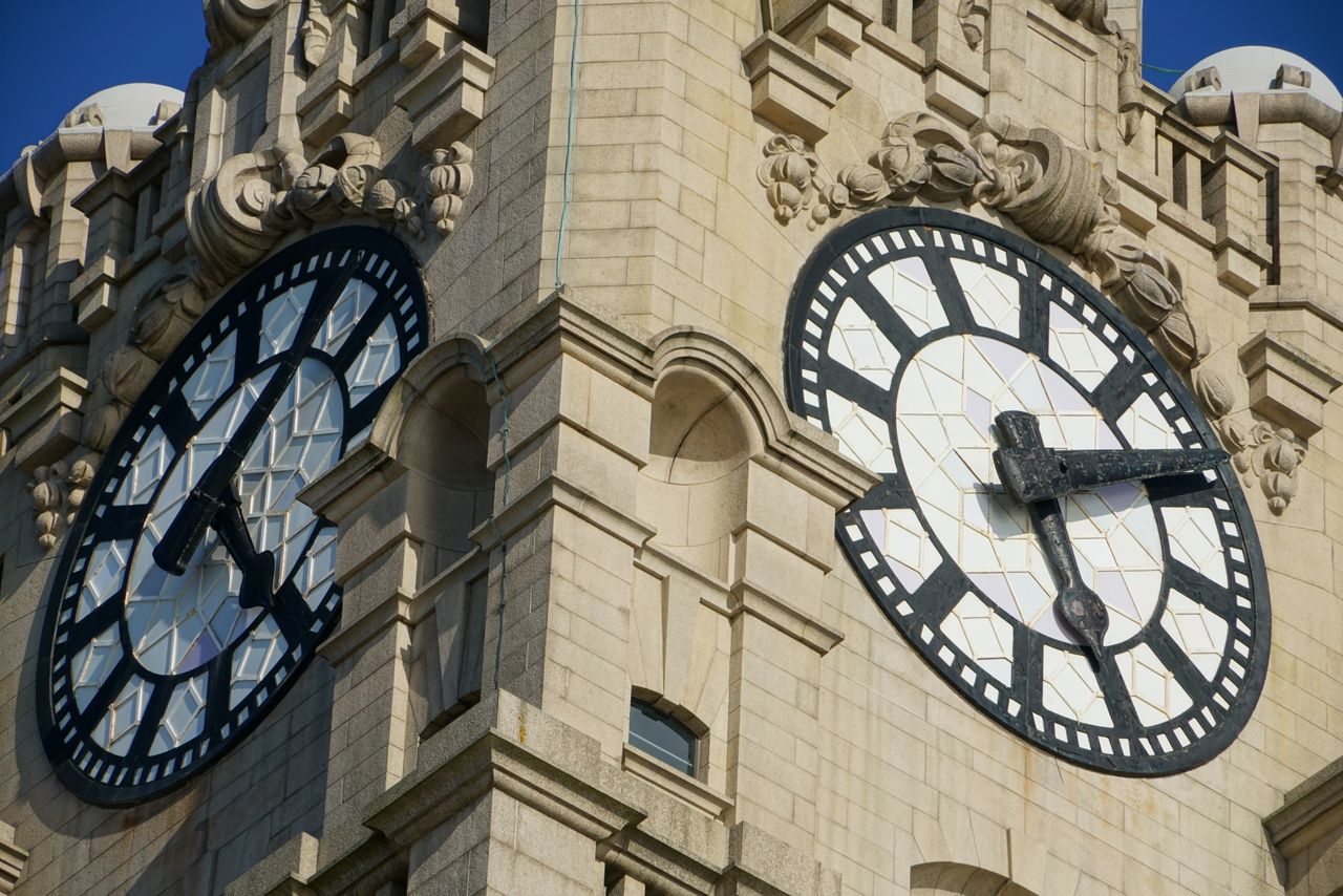 services-img Detailed view of ornate clock faces on a historic stone tower captured in bright sunlight.