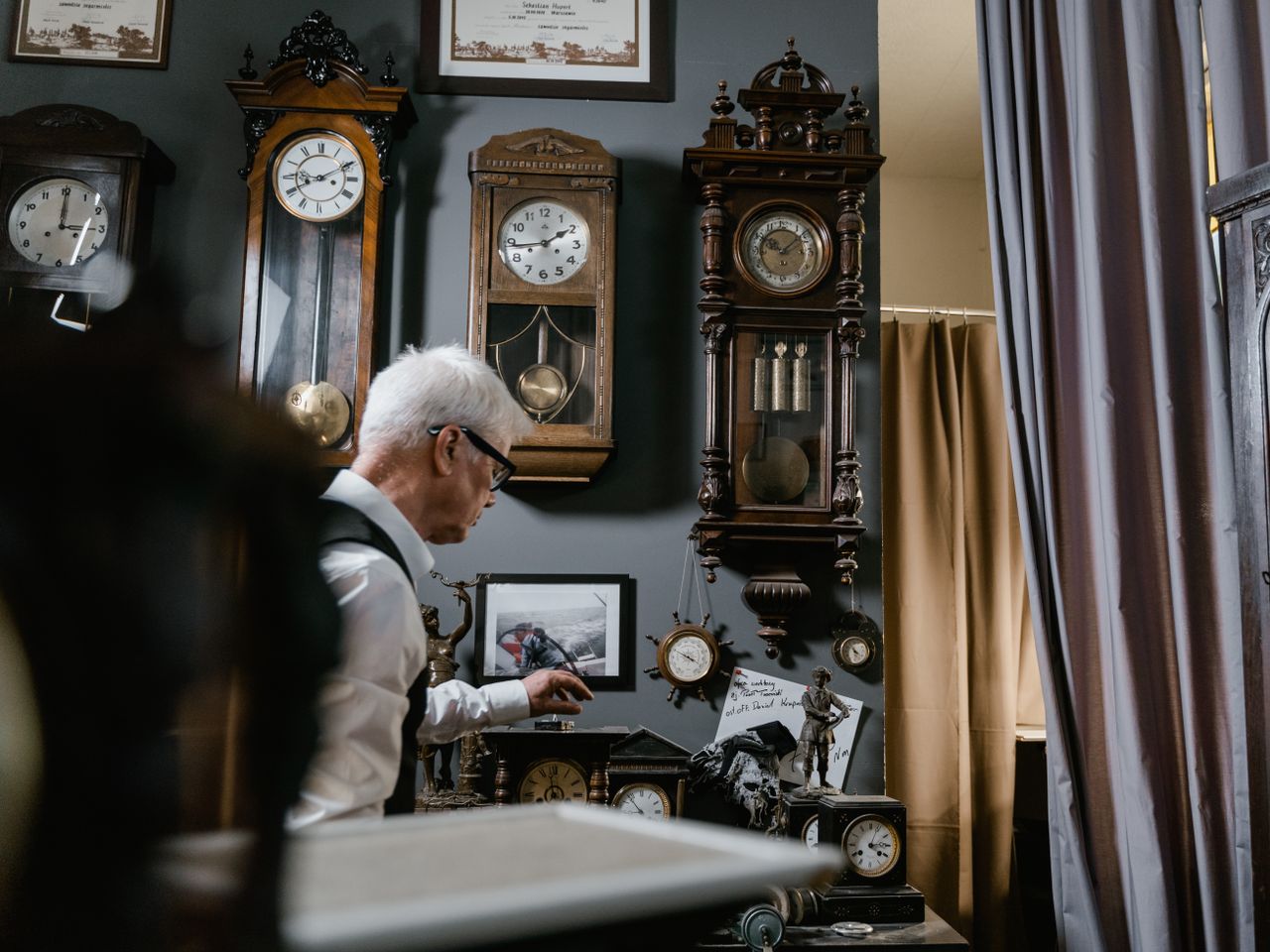 Watchmaker in vintage repair shop surrounded by antique wall clocks and intricate timepieces.